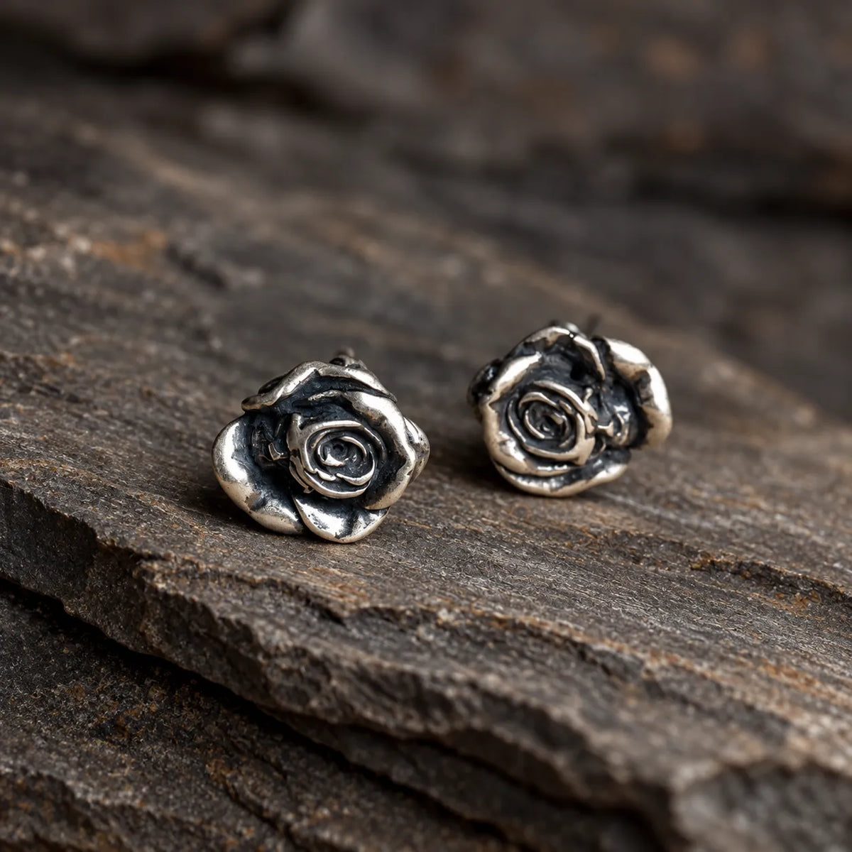 Close view of sculpted silver rose earrings with polished petals and oxidized recesses