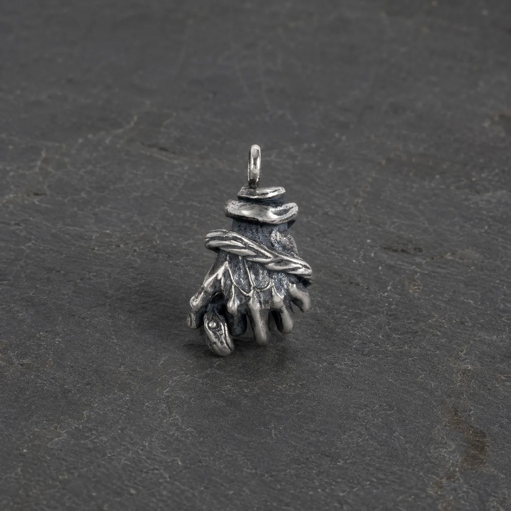 Oxidized 925 sterling silver serpent hand pendant displayed alone on dark stone
