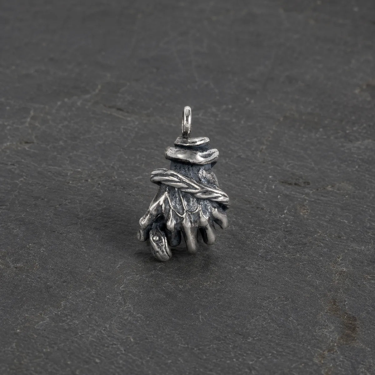 Oxidized 925 sterling silver serpent hand pendant displayed alone on dark stone