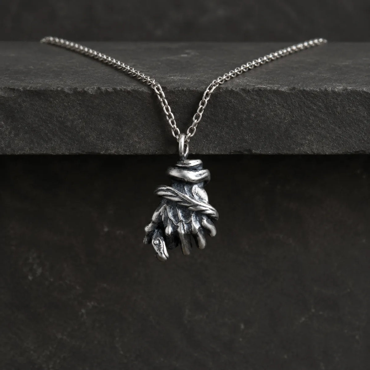 Serpent hand pendant hanging from an optional 2.0 mm chain over dark stone