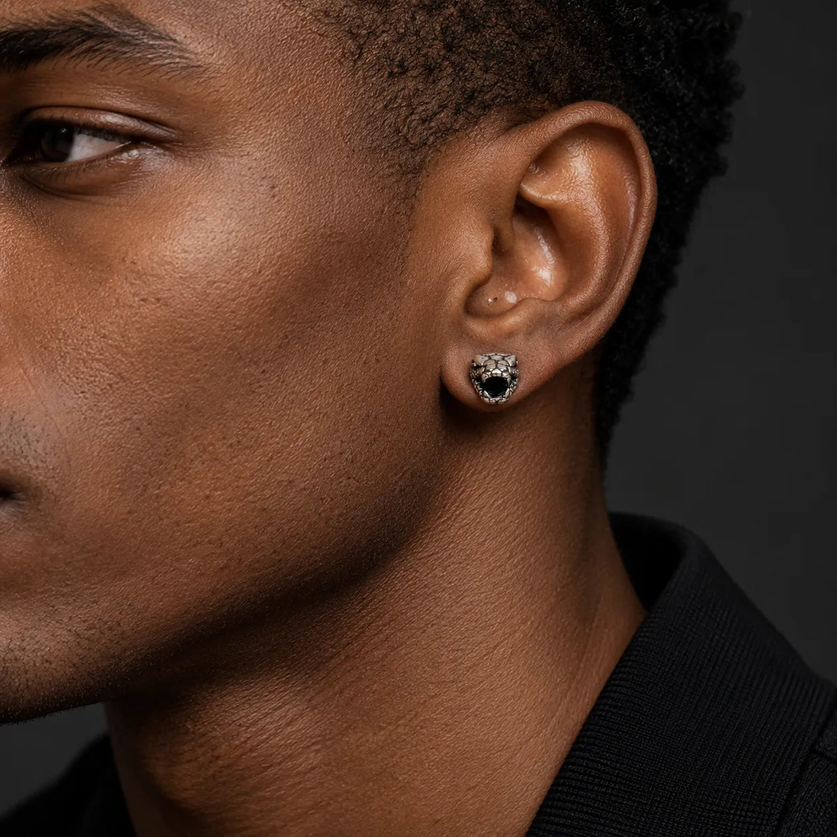 Small serpent head stud earring worn on an ear to show its approximately 5 by 6 mm face size