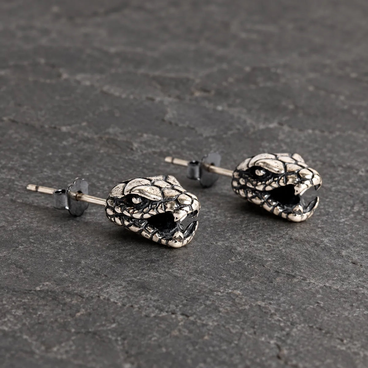 Three-quarter view of serpent head stud earrings showing their open jaws and sculptural depth
