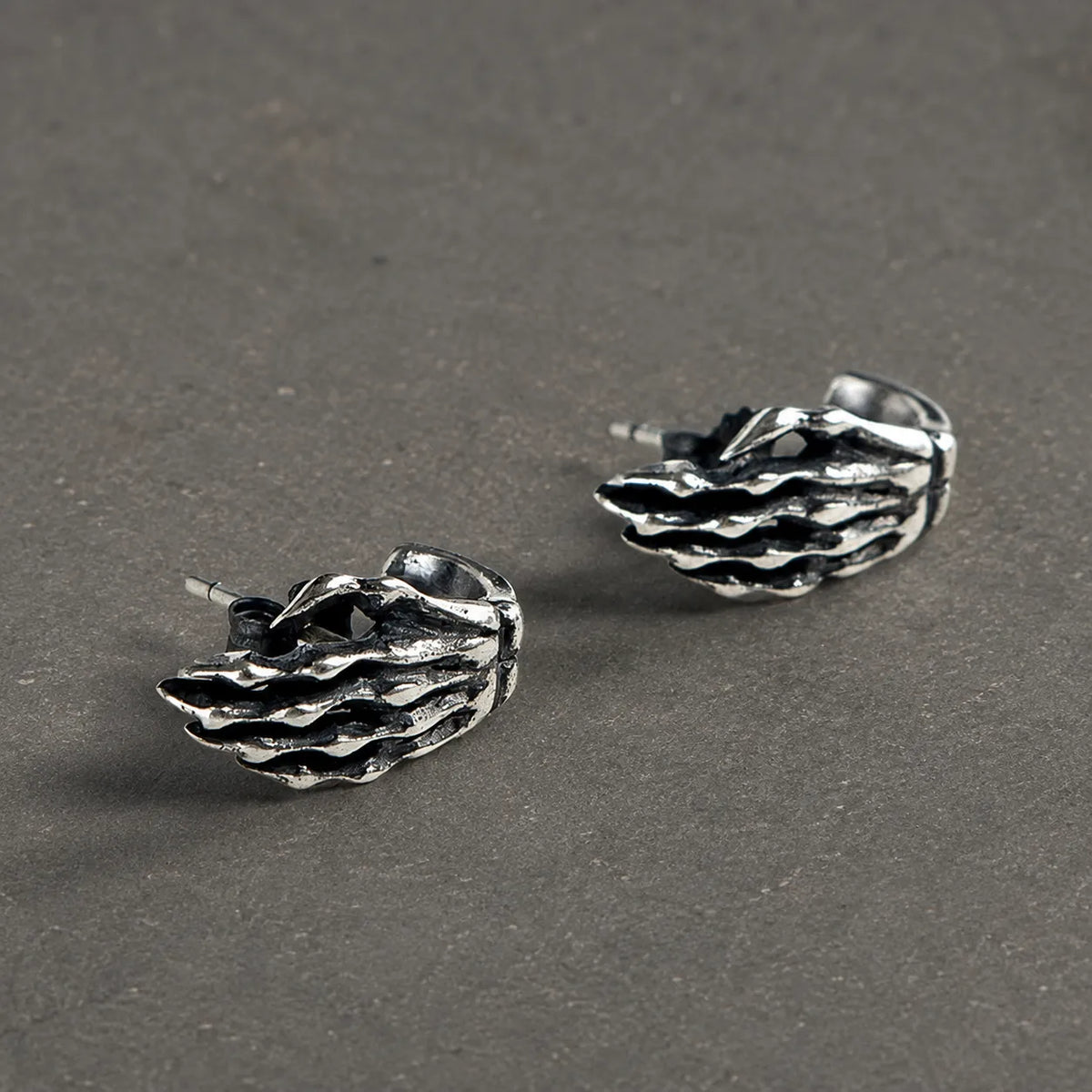 Pair of oxidized 925 sterling silver skeleton hand stud earrings on dark stone