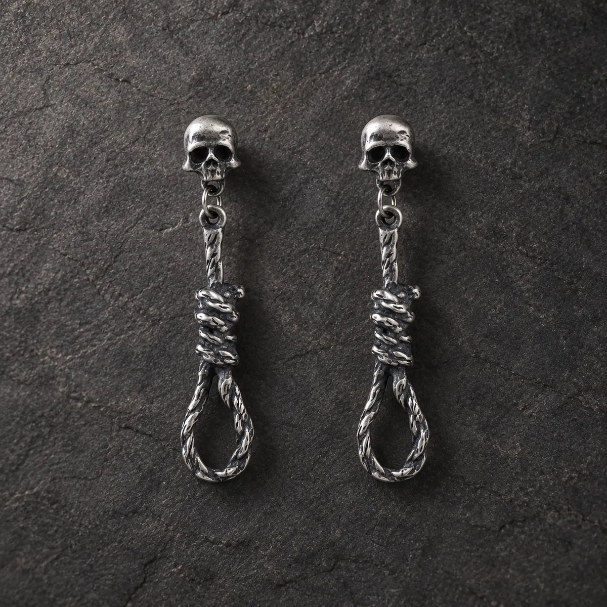 Pair of oxidized 925 sterling silver skull and noose dangle stud earrings on dark stone