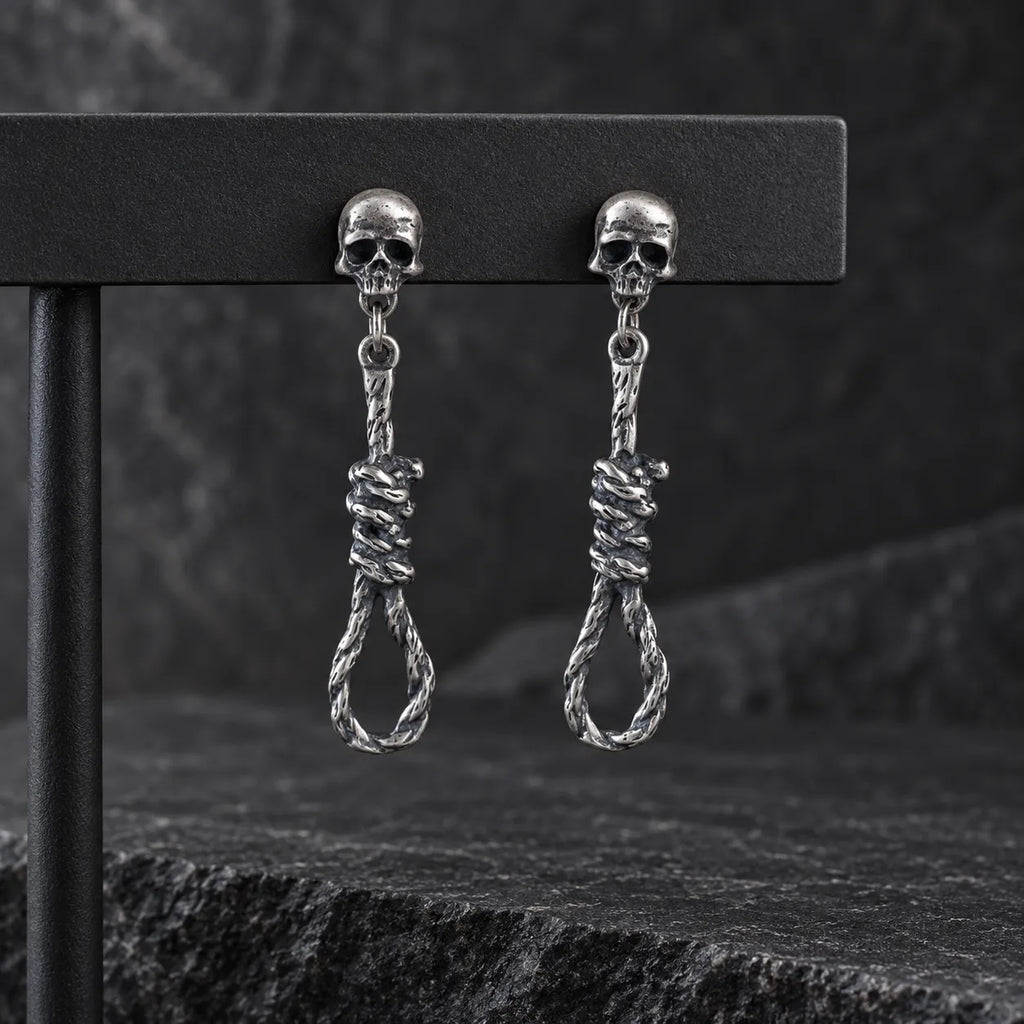 Pair of oxidized silver skull and noose earrings hanging from a dark jewelry display