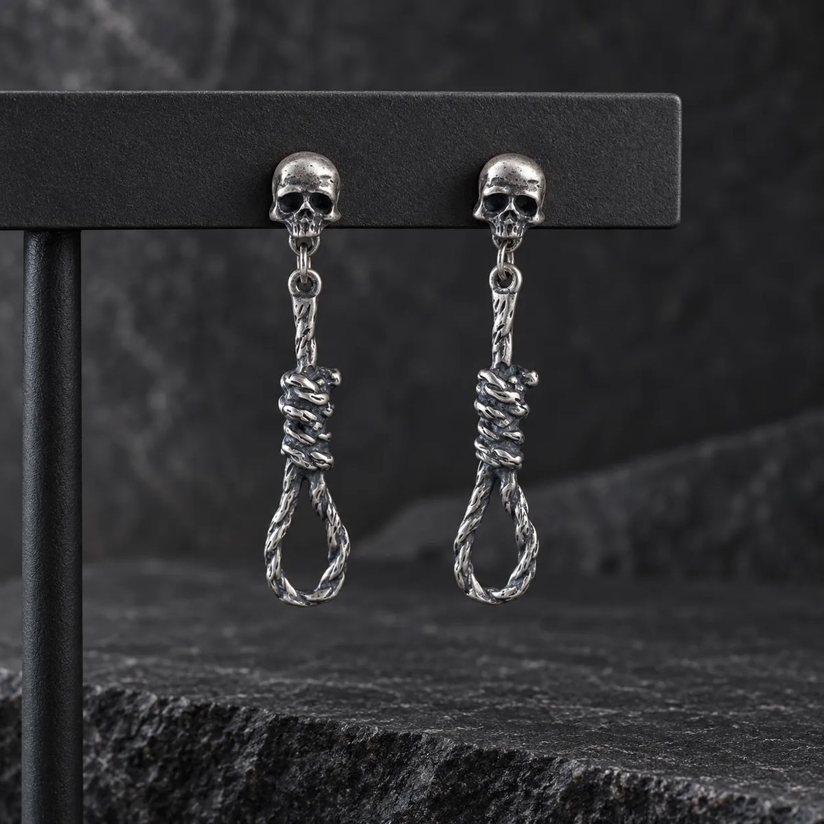 Pair of oxidized silver skull and noose earrings hanging from a dark jewelry display