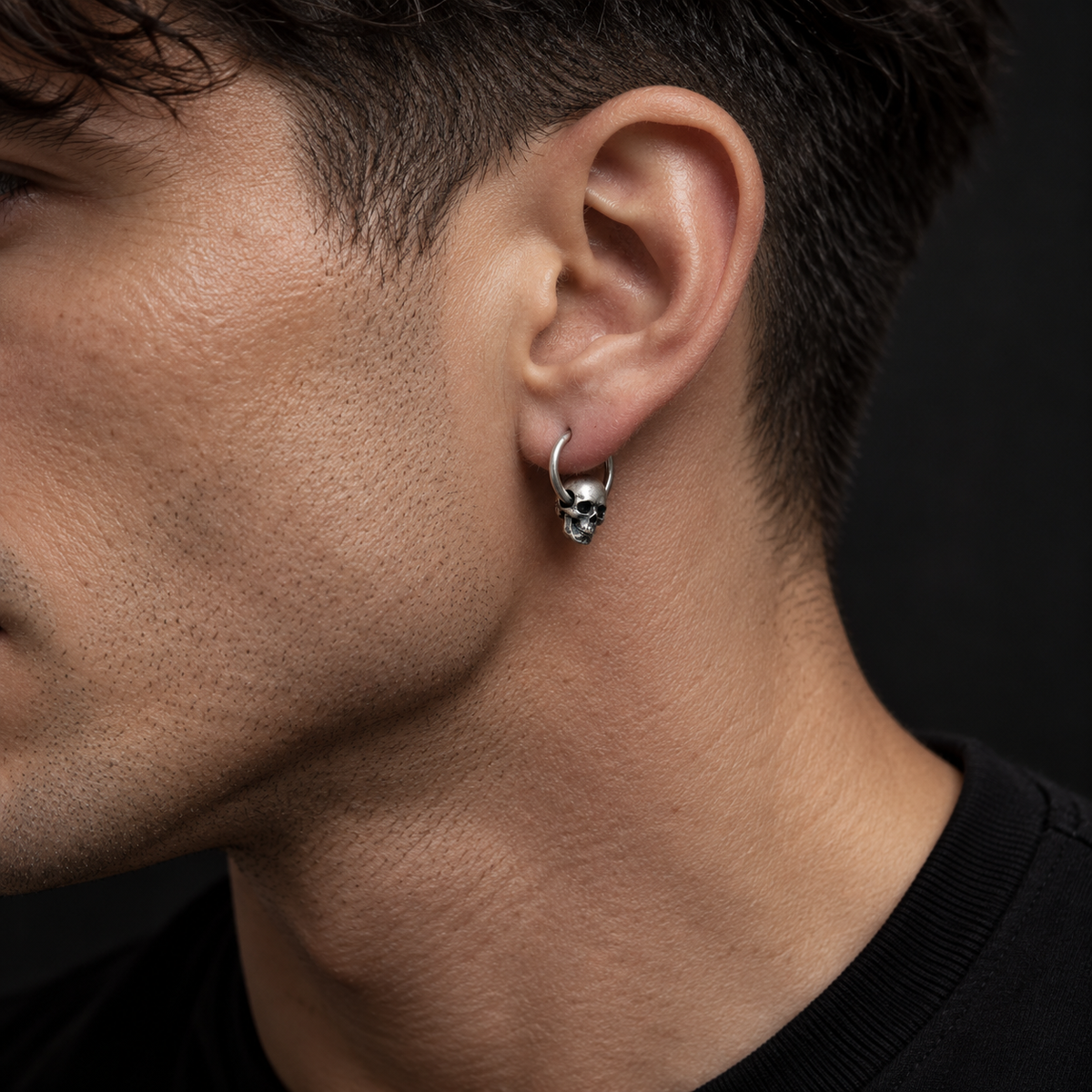 Male model wearing an oxidized sterling silver skull hoop earring at its actual 19 mm scale
