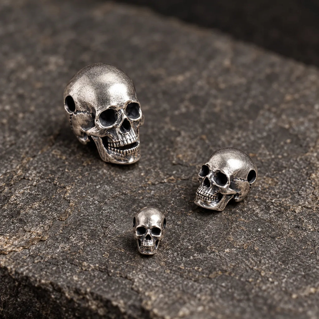 Three small articulated skull pendant sizes loosely arranged on textured dark stone