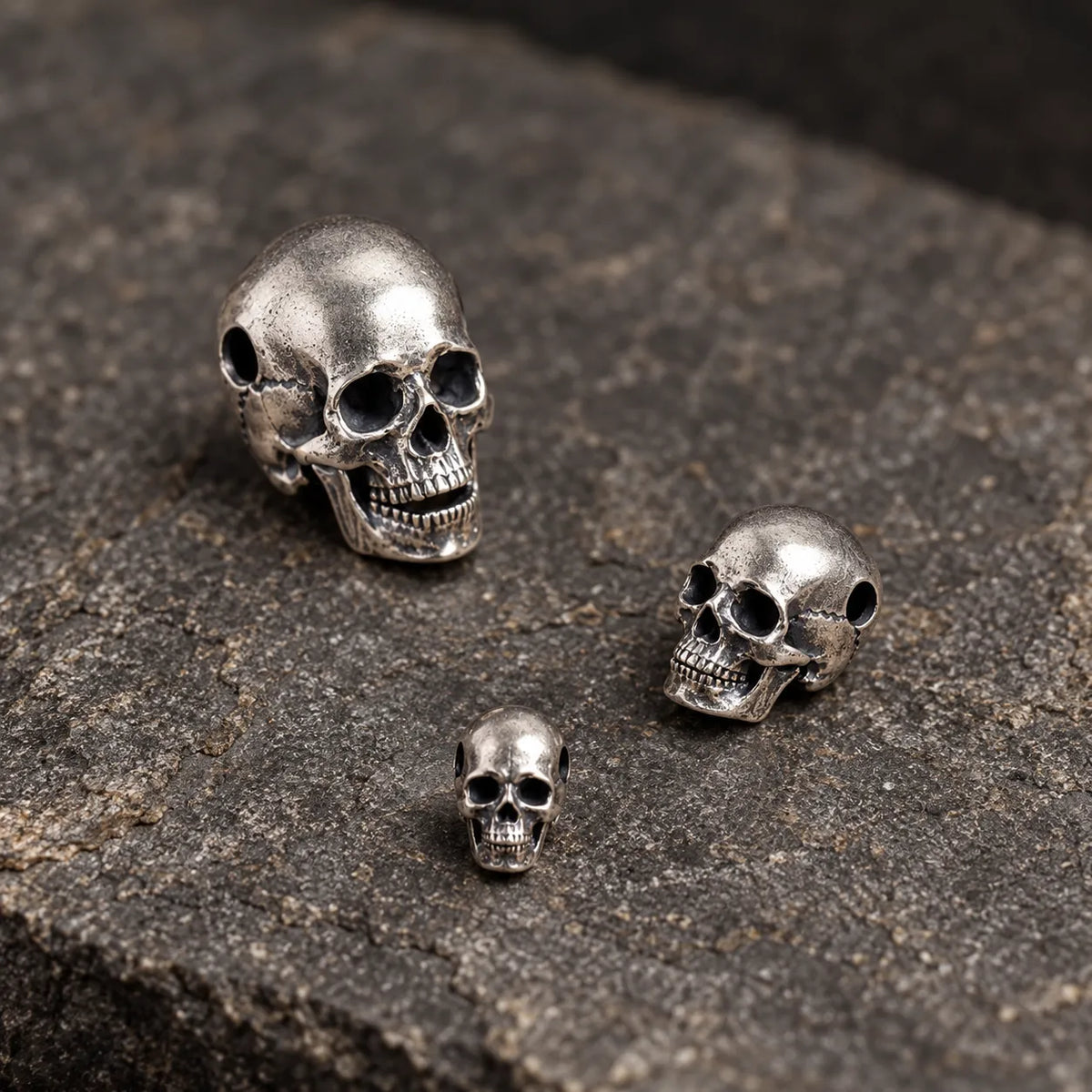 Three small articulated skull pendant sizes loosely arranged on textured dark stone