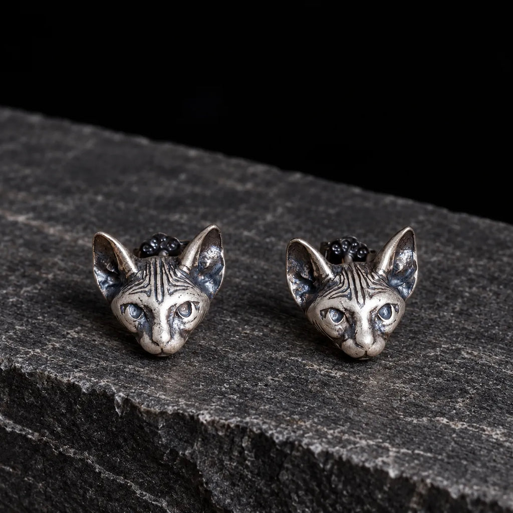 Oxidized silver Sphynx cat stud earrings displayed naturally on dark stone
