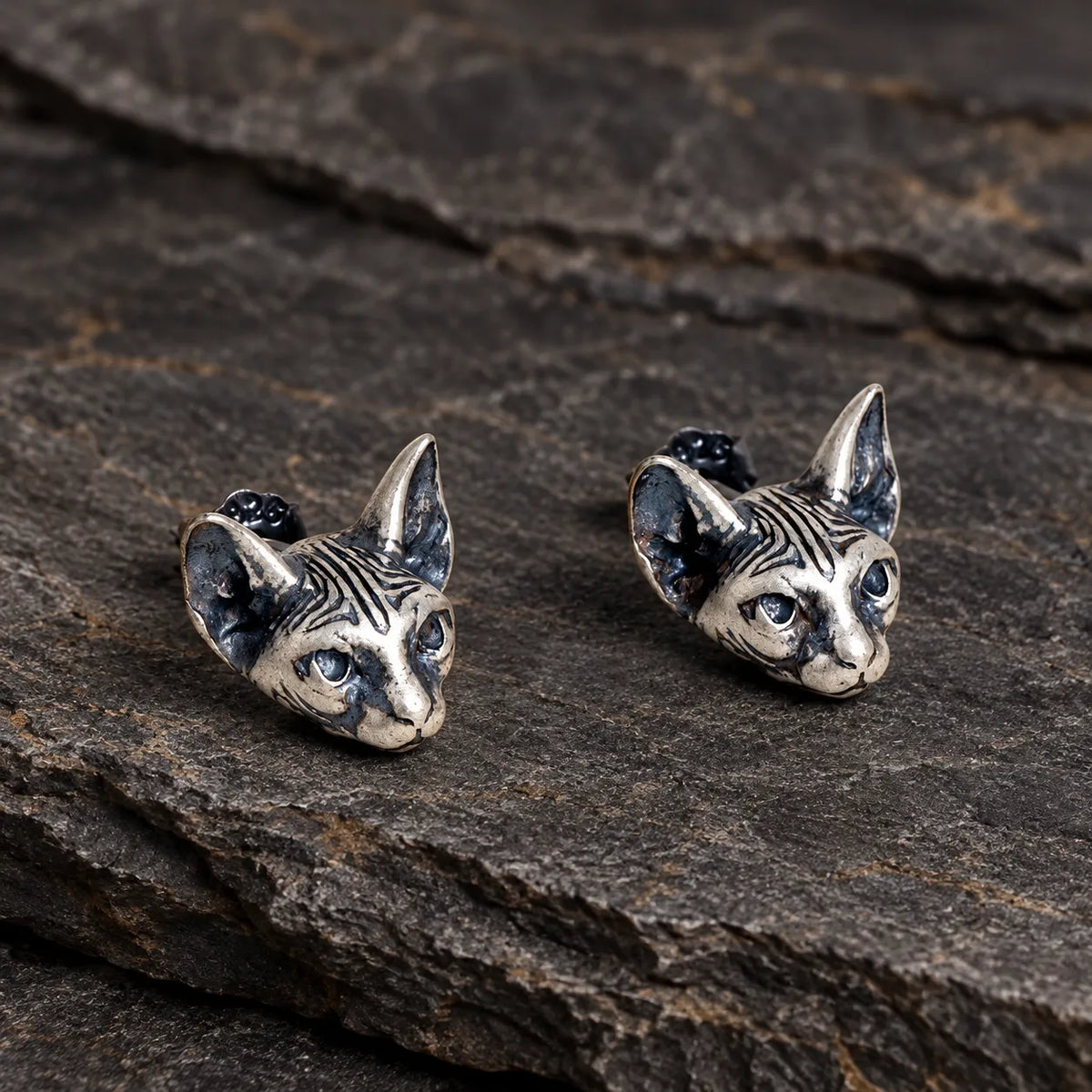 Three-quarter view of sculpted Sphynx cat stud earrings with dark oxidized details