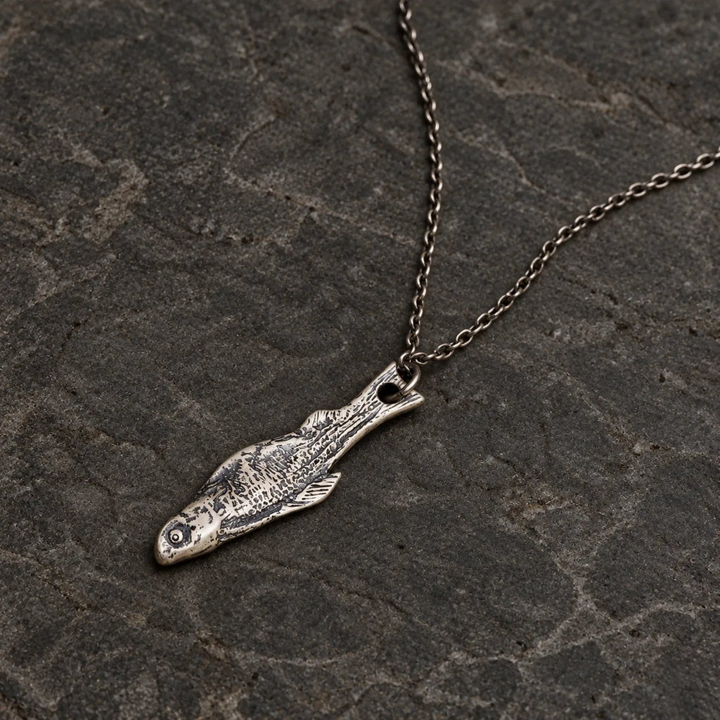 Flat lay of an oxidized sterling silver fish skeleton pendant with an optional 1.5 mm chain
