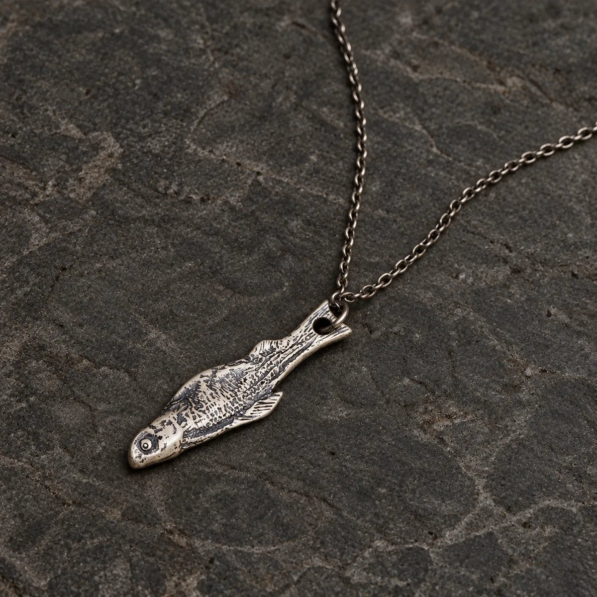 Flat lay of an oxidized sterling silver fish skeleton pendant with an optional 1.5 mm chain
