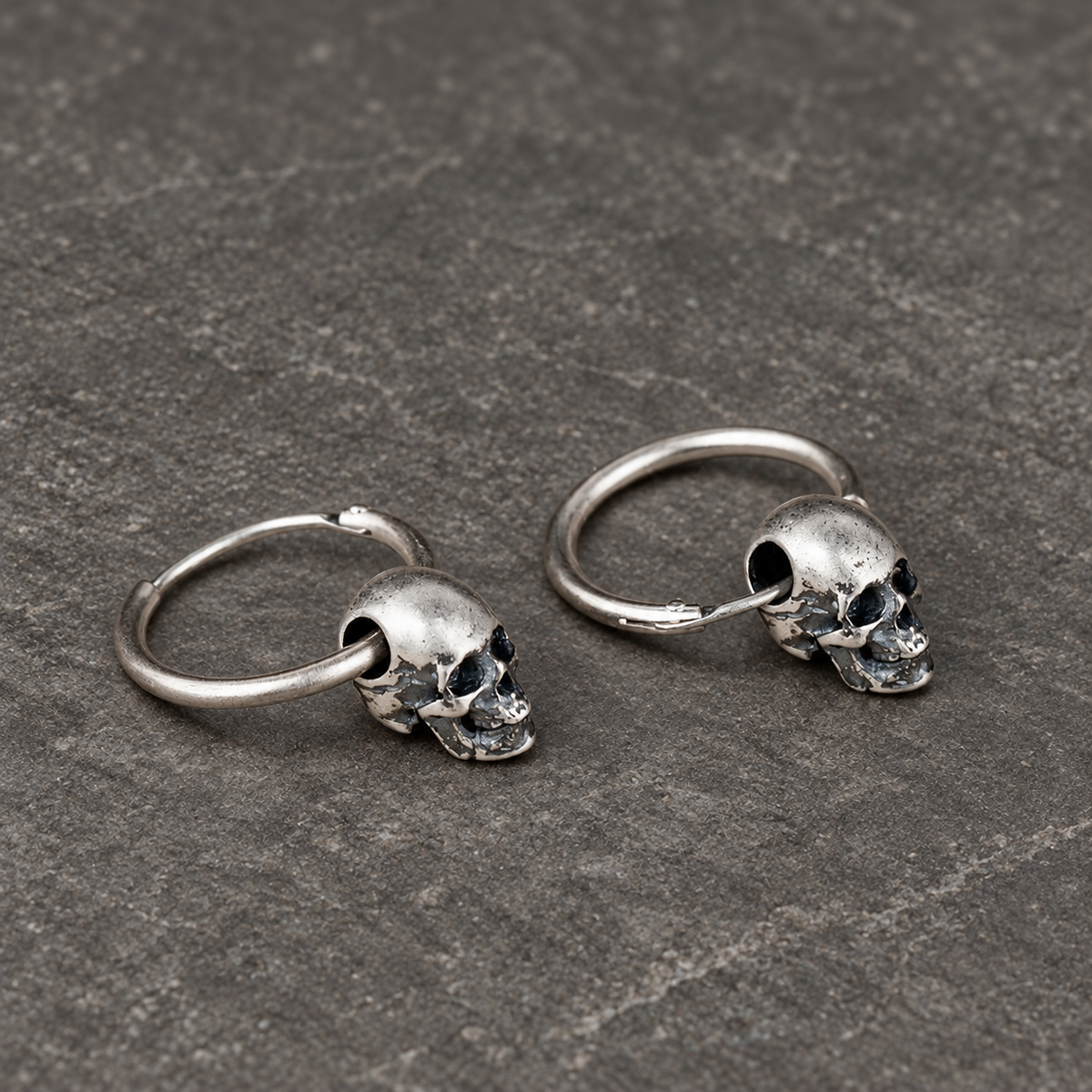 Angled view of sterling silver skull hoop earrings showing their curved wire construction