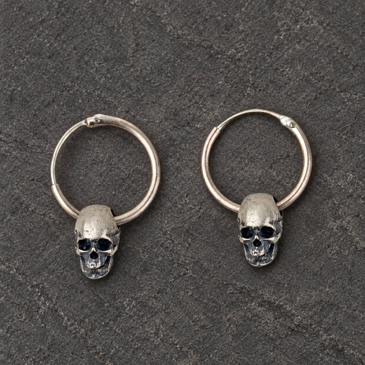 Pair of oxidized sterling silver skull hoop earrings shown from the front