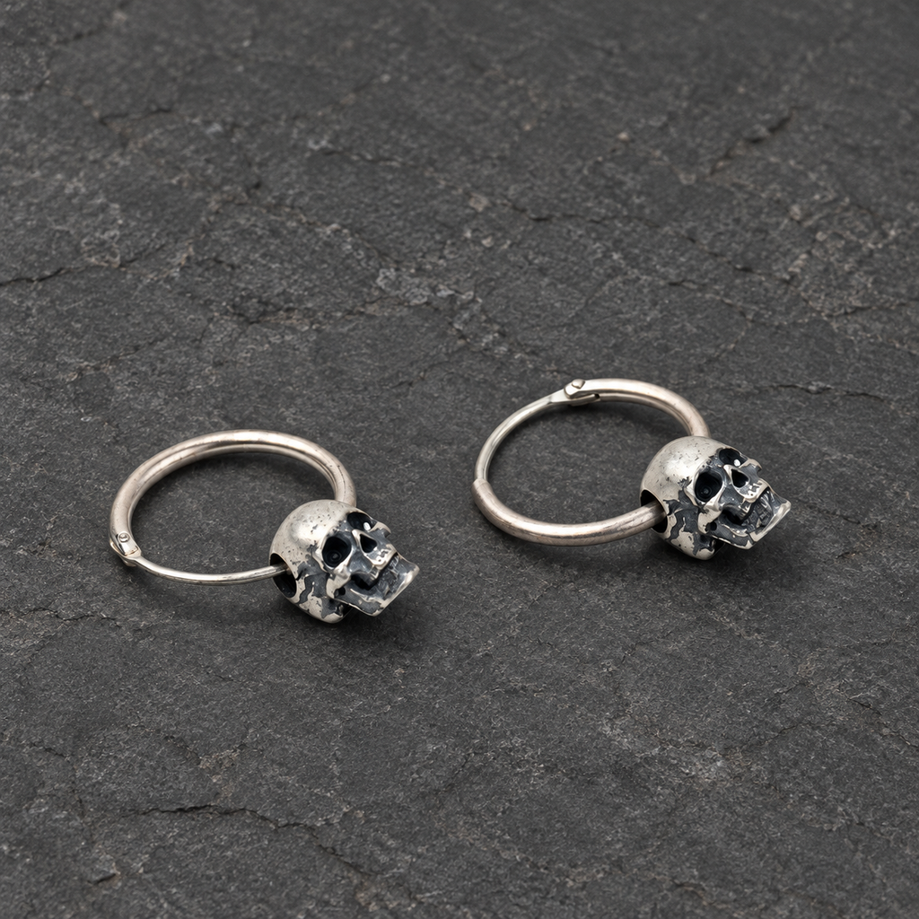 Three-quarter view of a pair of oxidized silver skull hoop earrings