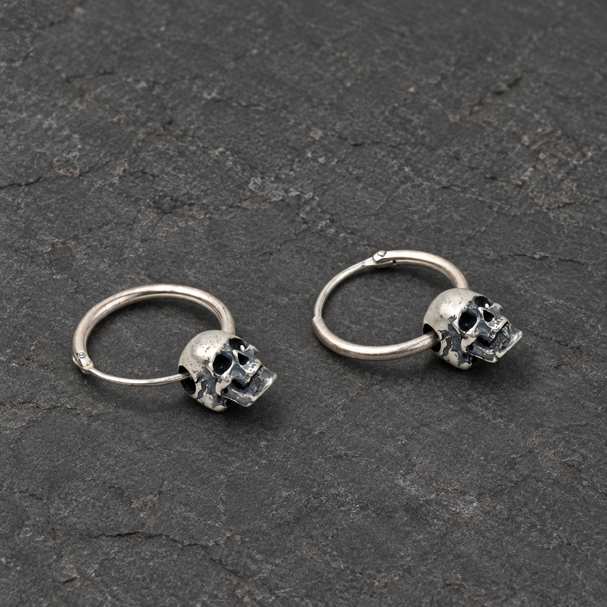 Three-quarter view of a pair of oxidized silver skull hoop earrings