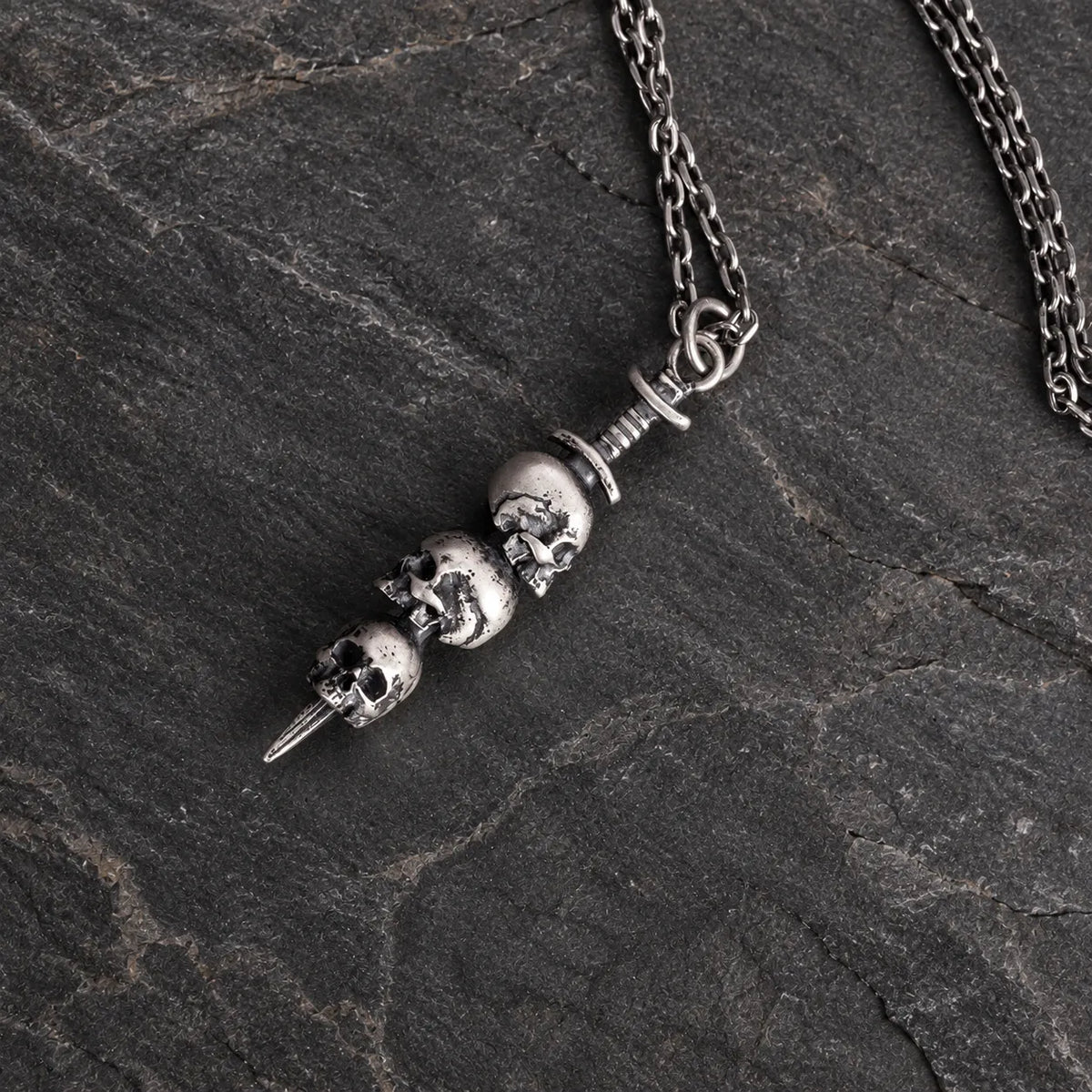 Oxidized silver triple skull dagger pendant displayed with an optional 2.0 mm chain