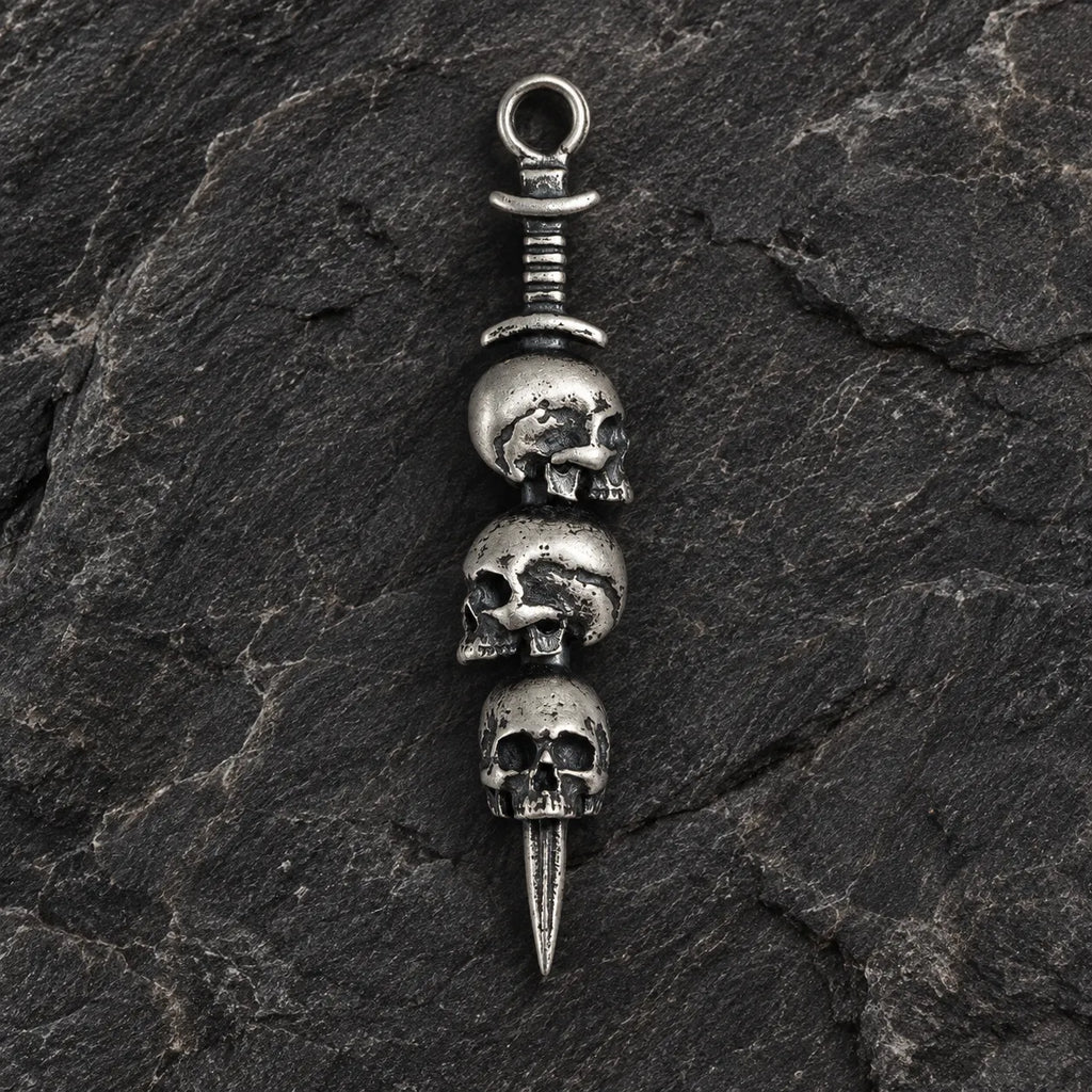 Front view of an oxidized 925 sterling silver triple skull dagger pendant on dark stone