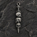 Front view of an oxidized 925 sterling silver triple skull dagger pendant on dark stone