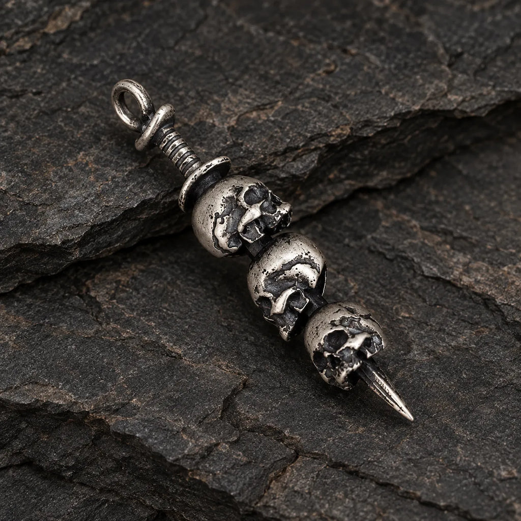 Three-quarter view of a triple skull dagger pendant showing its sculptural depth and pointed blade