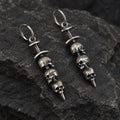Angled view of triple skull sword earrings showing their sculptural depth and wire hoops