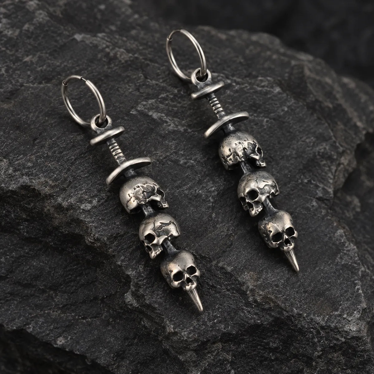 Angled view of triple skull sword earrings showing their sculptural depth and wire hoops