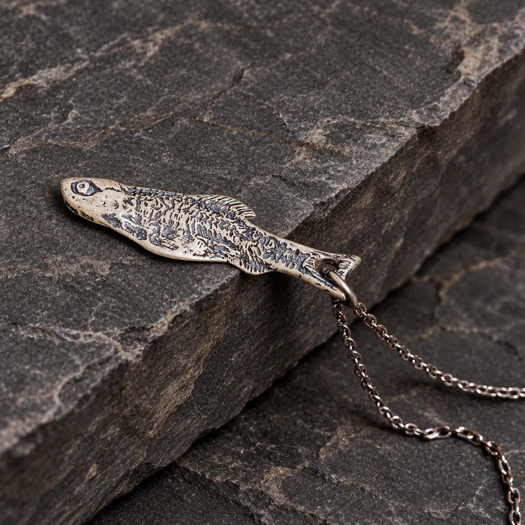 Close angled view of a solid fish pendant with dark skeletal engravings on stone