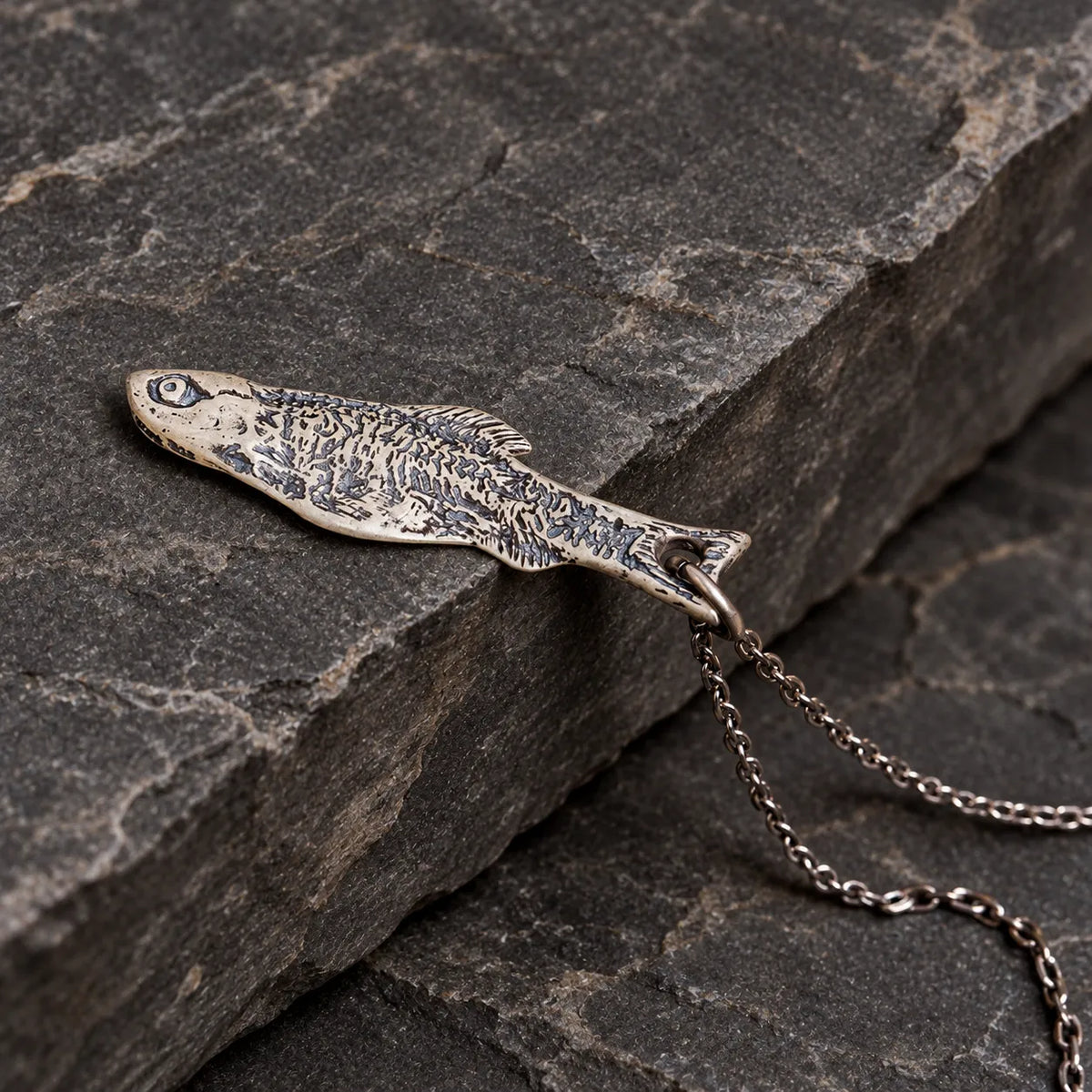 Close angled view of a solid fish pendant with dark skeletal engravings on stone